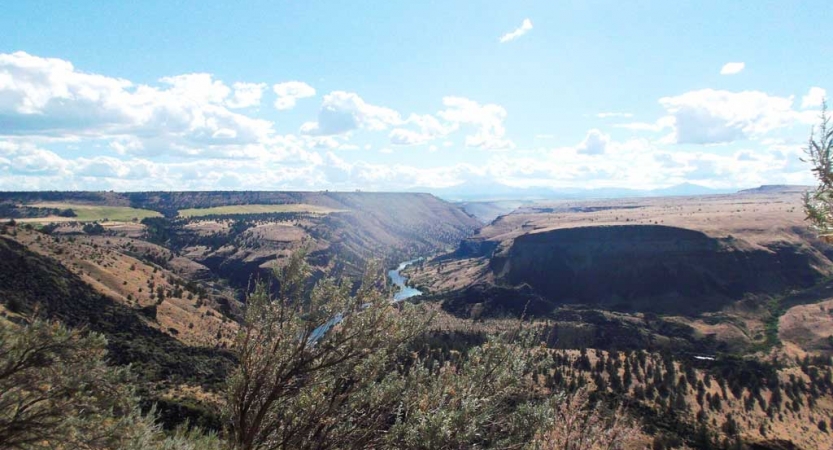 a river flows through a vast hilly landscape under blue skies